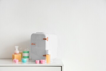 Obraz na płótnie Canvas Small cosmetic refrigerator and products on shelf near light wall