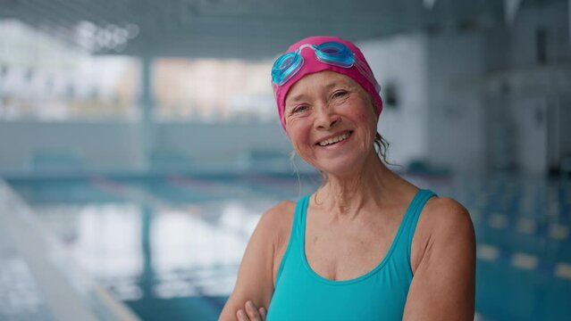 Happy senior woman after swim looking at camera in indoors swimming pool.