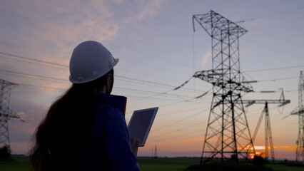 Woman power engineer in a white helmet checks power line using data from electrical sensors on a...