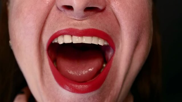 Close-up of the face of a caucasian woman with lips painted with red lipstick sings song, opening her mouth wide on a black background.