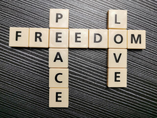 Crossword freedom peace love made from square letter tiles against black background.