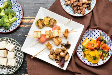 Composition with grilled tofu cheese skewers and vegetables on dark wooden background