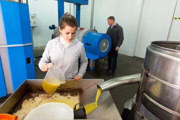 Skilled woman engaged in traditional olive oil production inspecting first pressing of olives and oil decanting