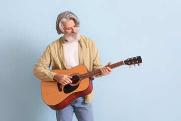 Bearded senior man playing guitar on blue background