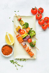 Plate with tasty vegetable skewers and spices on light background