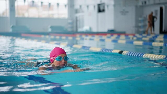 Active senior woman swimming in indoors swimming pool.