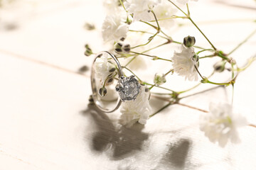 Beautiful silver engagement ring with white flowers on light background, closeup