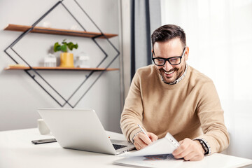 A happy entrepreneur sitting at his home office and working on paperwork.