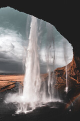 View of Seljalandsfoss from Rock Hangover behind waterfall with a rainbow forming in Southern Region of Iceland