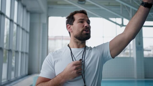 Personal coach whistling and giving instructions indoors in swimming pool.