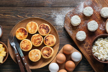 Plate with tasty cottage cheese pancakes and ingredients on wooden background