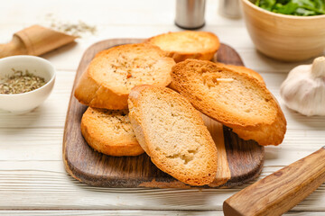 Board of tasty croutons on white wooden background