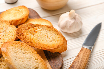 Board of tasty croutons on white wooden background, closeup