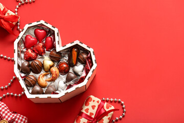 Naklejka premium Heart shaped box with tasty chocolate candies on red background