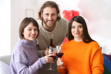 Man and two beautiful women drinking wine at home. Concept of polyamory