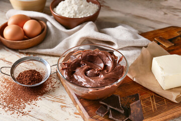 Bowl with fresh dough and ingredients for preparing chocolate brownie on white wooden background