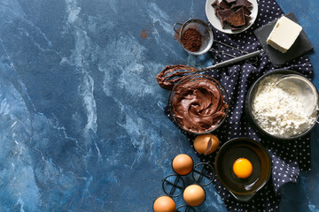 Bowl with fresh dough and ingredients for preparing chocolate brownie on blue background