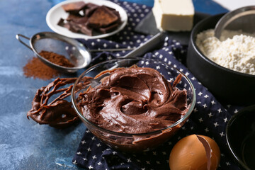 Bowl with fresh dough and ingredients for preparing chocolate brownie on blue background