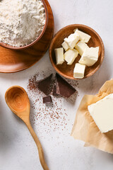 Bowl with pieces of butter and ingredients for preparing chocolate brownie on white background