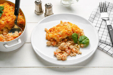 Plate and baking dish with tasty English fish pie on white wooden background