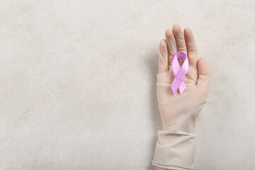 Hand in medical glove with awareness ribbon on light background. Concept of World Cancer Day