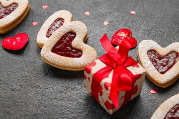 Tasty cookies in heart shape and gift box on dark background