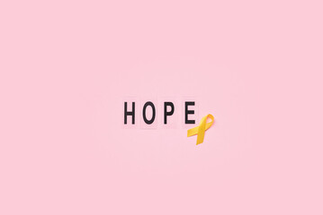 Golden awareness ribbon and word HOPE on pink background. International Childhood Cancer Day