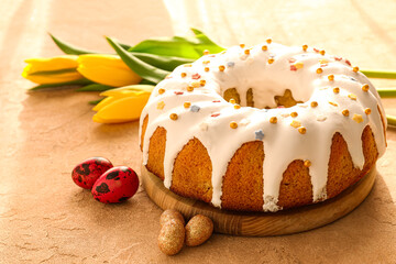 Wooden board with tasty Easter cake and eggs on beige background
