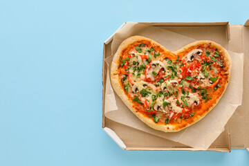 Cardboard box with tasty heart-shaped pizza on blue background. Valentine's Day celebration