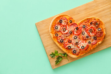 Wooden board with tasty heart-shaped pizza on green background. Valentine's Day celebration