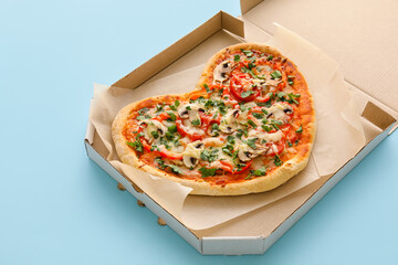 Cardboard box with tasty heart-shaped pizza on blue background. Valentine's Day celebration