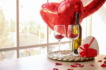 Tray with bottle of wine, glasses and gift box for Valentine's Day celebration on windowsill