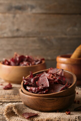 Plates with spicy beef jerky on wooden background