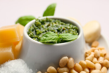 Bowl of pesto sauce and ingredients on light background