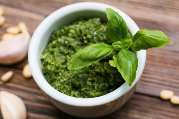 Bowl of tasty pesto sauce and ingredients on wooden background