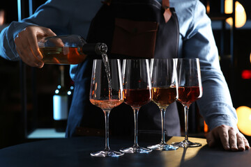 Bartender pouring rose wine from bottle into glass at table indoors, closeup