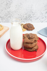 Galletas de chocolate en vertical con vaso de leche leche sobre plato rojo
