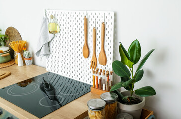 Peg board with spatulas, bottle of oil and napkin hanging on green wall