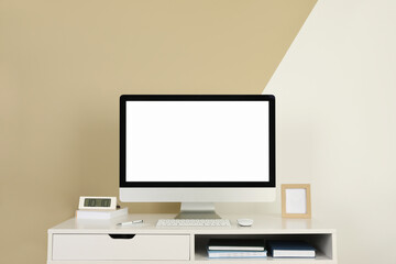 Modern computer, digital clock and office supplies on white wooden table near color wall