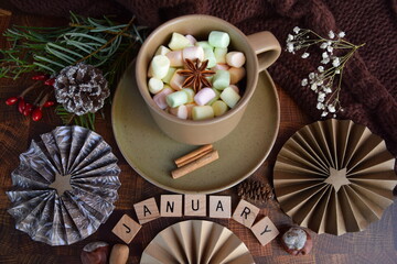 Fototapeta na wymiar Still life with handmade rosettes, cup of marshmallows, word January and greenery on table. 