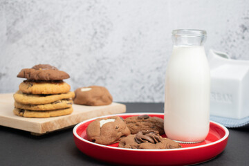 Galletas de chocolate con vaso de leche sobre plato rojo 