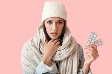 Young woman with sick throat holding blisters with pills on color background