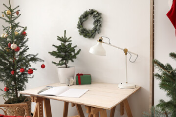 Workplace with opened notebook and Christmas trees near light wall in room