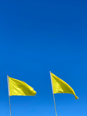Two yellow flags on a clear, blue sky background