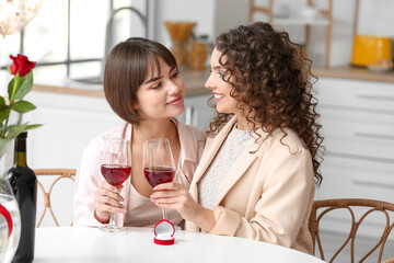 Happy engaged lesbian couple drinking wine at home