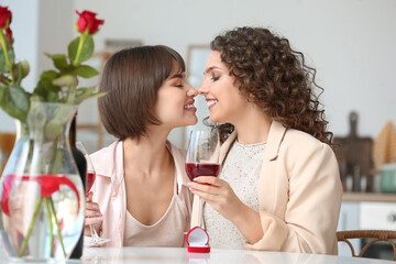 Happy engaged lesbian couple drinking wine at home