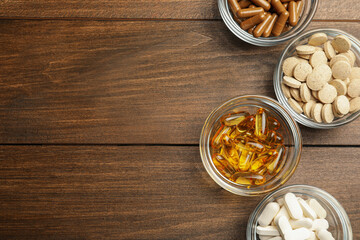 Fototapeta na wymiar Different dietary supplements in glass bowls on wooden table, flat lay. Space for text