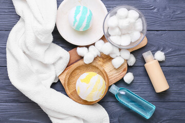 Bowl with cotton balls, cosmetics and bath bombs on grey wooden background