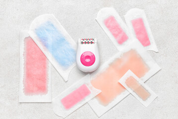 Modern epilator and wax strips on light background