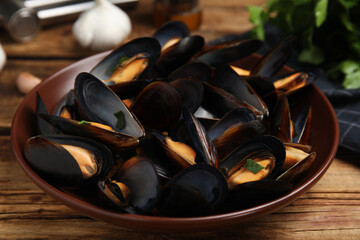 Plate of cooked mussels with parsley on wooden table, closeup